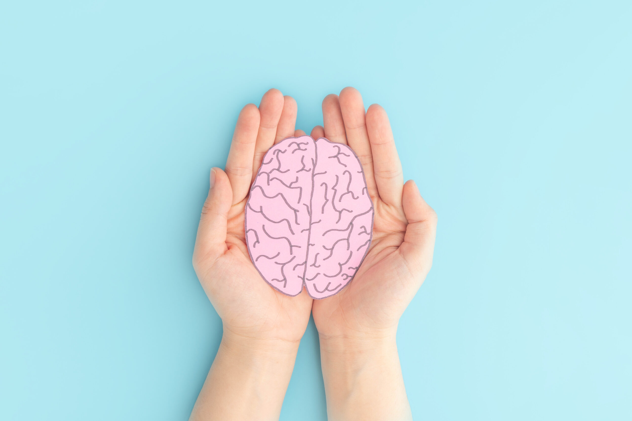 Woman hands holding human brain shape made from paper on light blue background. Awareness of Alzheimer, Parkinson’s disease, dementia, stroke, seizure or mental health. Neurology and Psychology care.